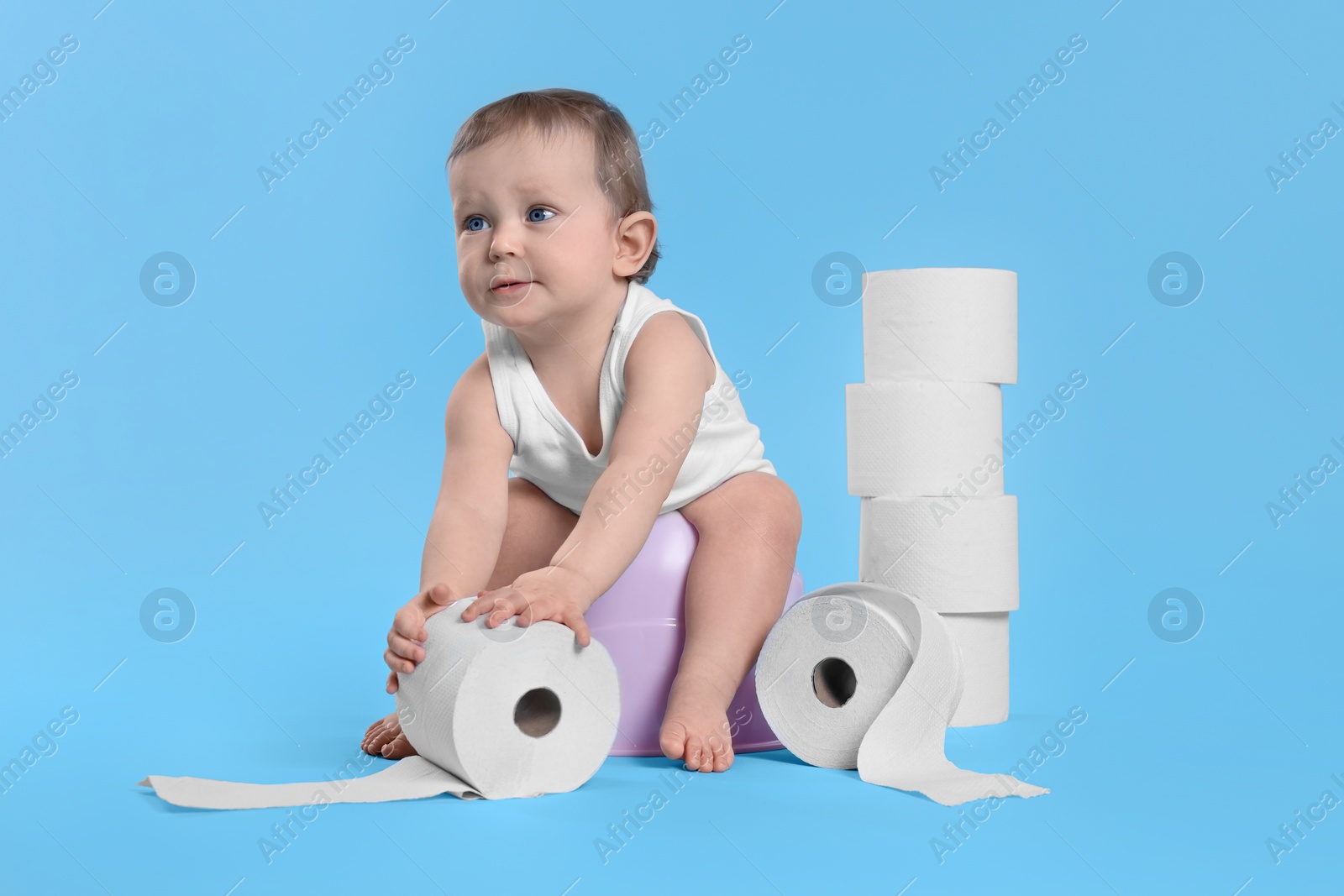 Photo of Little child sitting on baby potty and stack of toilet paper rolls against light blue background