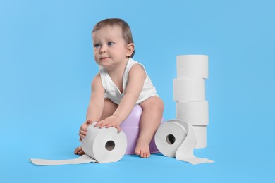 Photo of Little child sitting on baby potty and stack of toilet paper rolls against light blue background