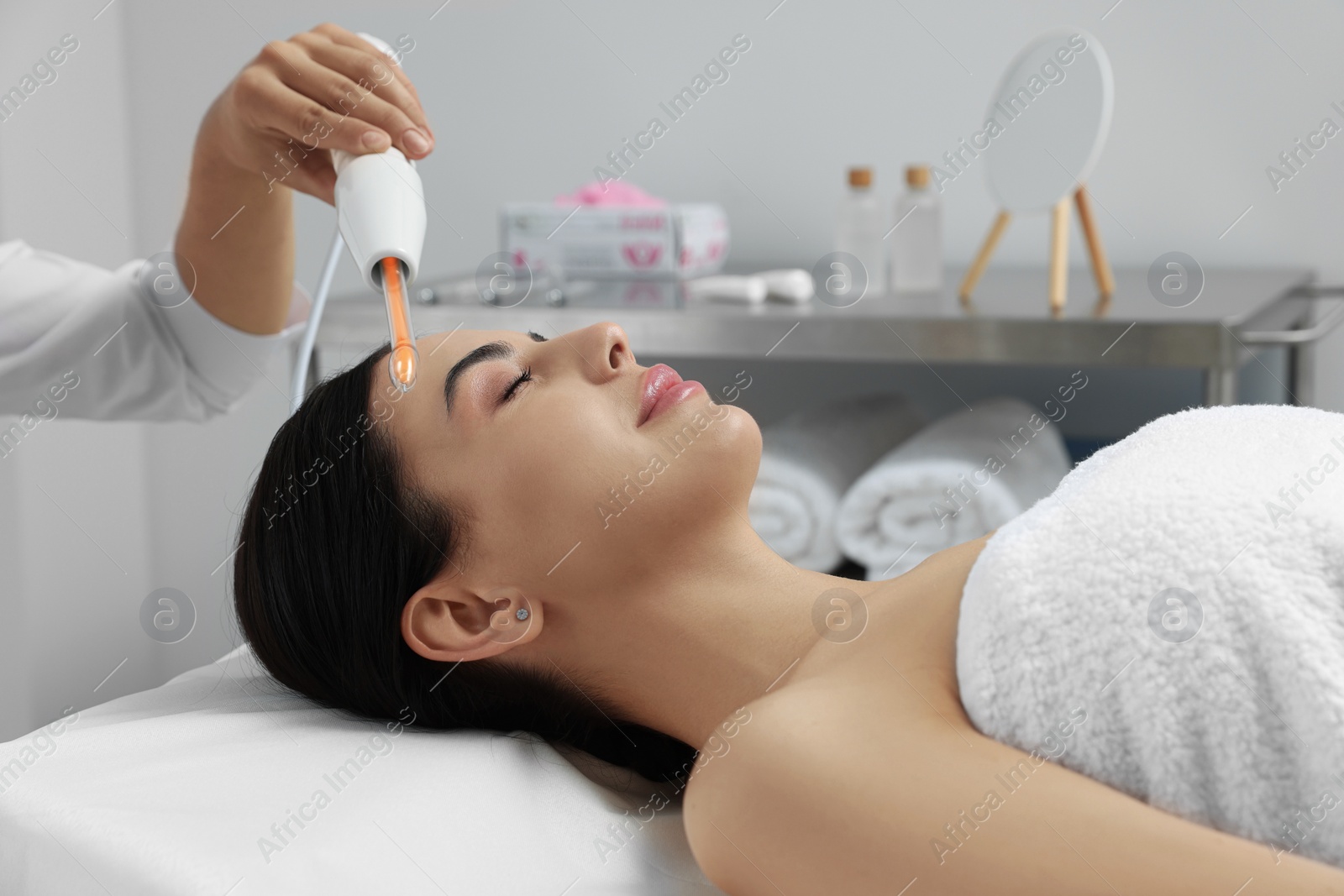 Photo of Young woman undergoing face rejuvenation procedure with darsonval in salon