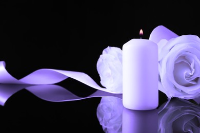 Violet roses and burning candle on black mirror surface, space for text. Funeral attributes