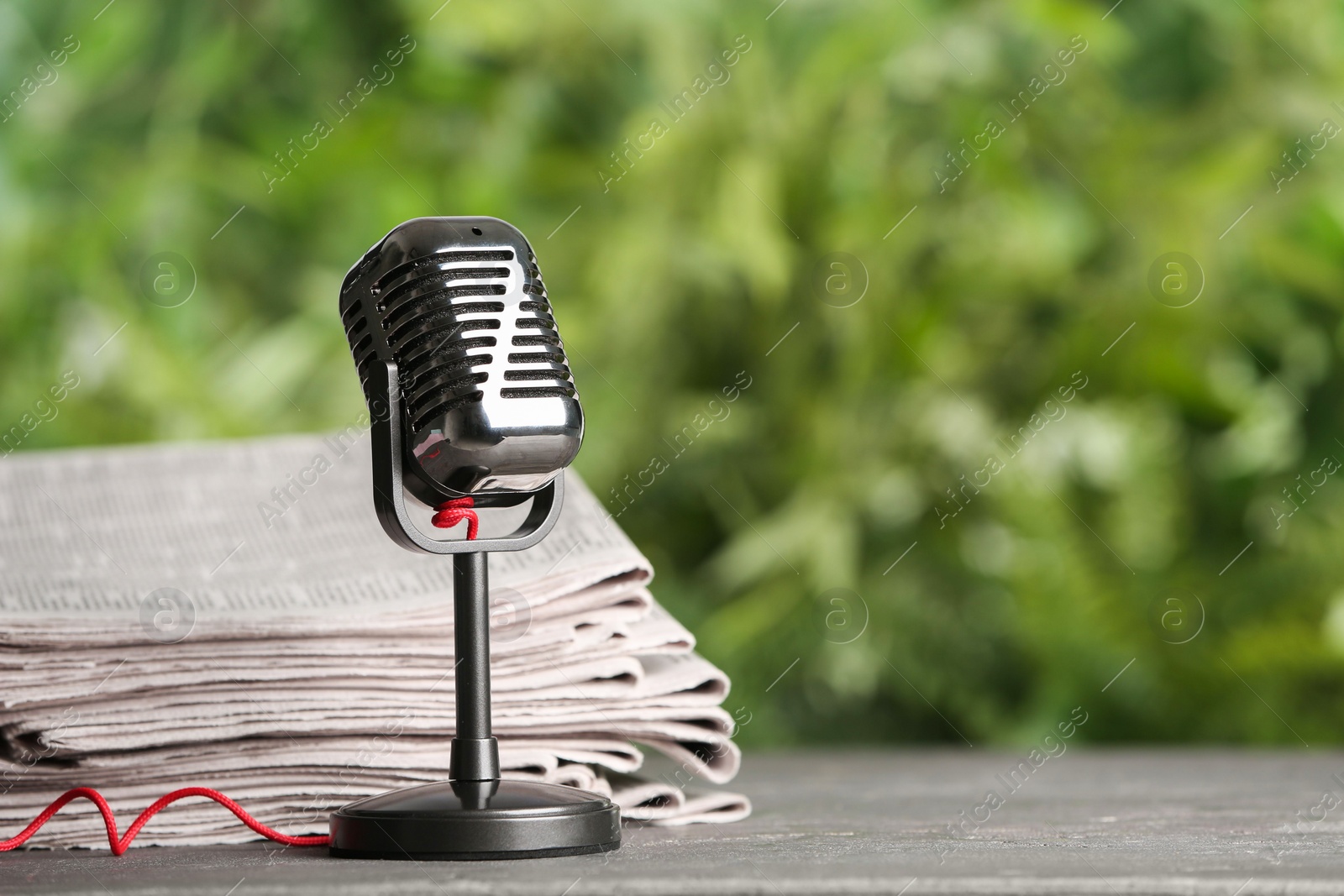 Photo of Newspapers and vintage microphone on grey table against blurred green background, space for text. Journalist's work