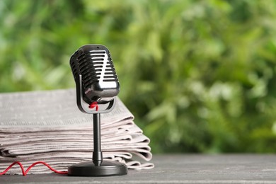 Newspapers and vintage microphone on grey table against blurred green background, space for text. Journalist's work
