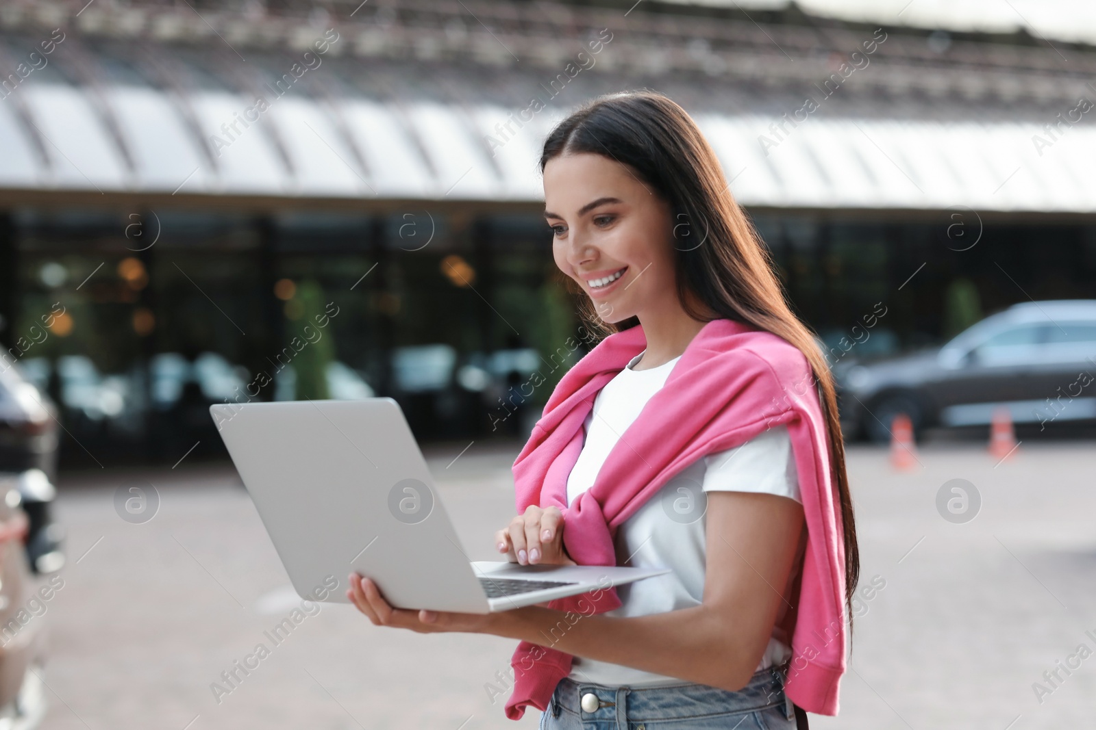 Photo of Happy young woman using modern laptop on city street