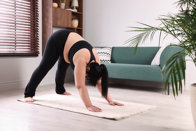 Photo of Overweight mature woman practicing yoga on rug at home