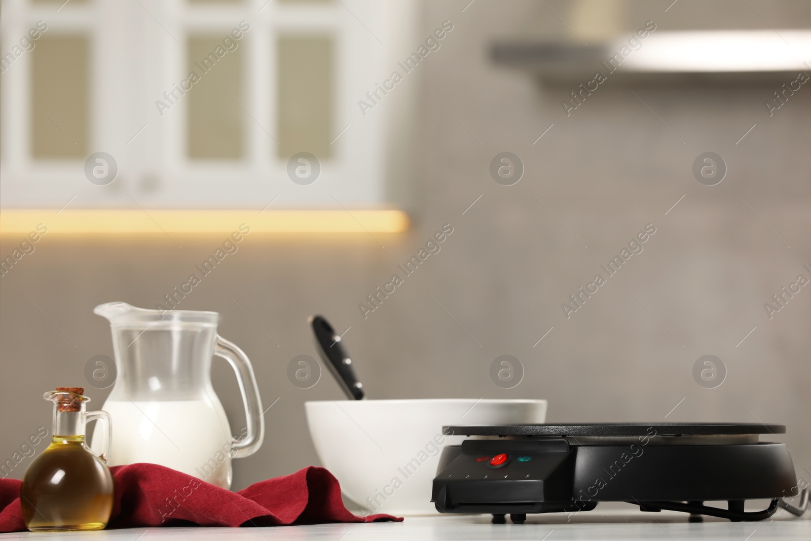 Photo of Electrical crepe maker and ingredients on white marble table in kitchen, space for text