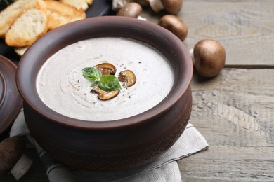 Photo of Fresh homemade mushroom soup in ceramic pot on wooden table, closeup. Space for text