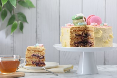 Photo of Delicious cake decorated with macarons and marshmallows and tea served on white marble table