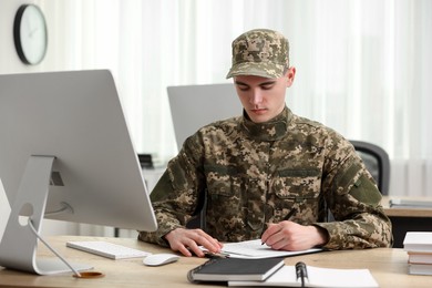 Military service. Young soldier working at wooden table in office