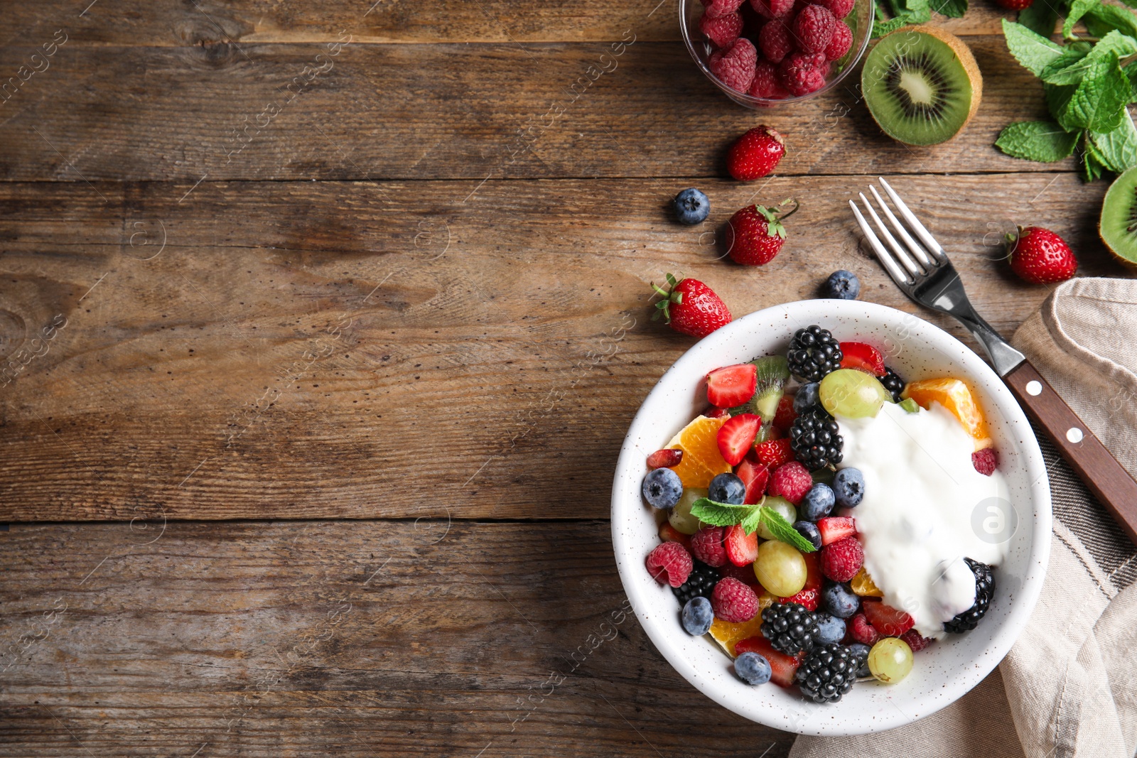 Photo of Fresh tasty fruit salad with yogurt on wooden table, flat lay. Space for text