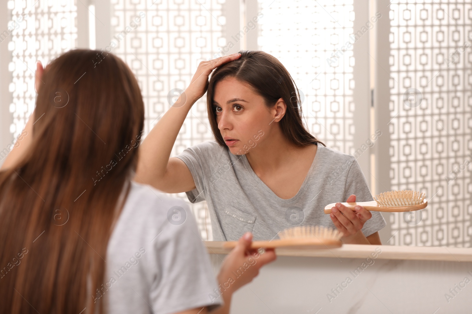 Photo of Young woman with hair loss problem looking in mirror indoors