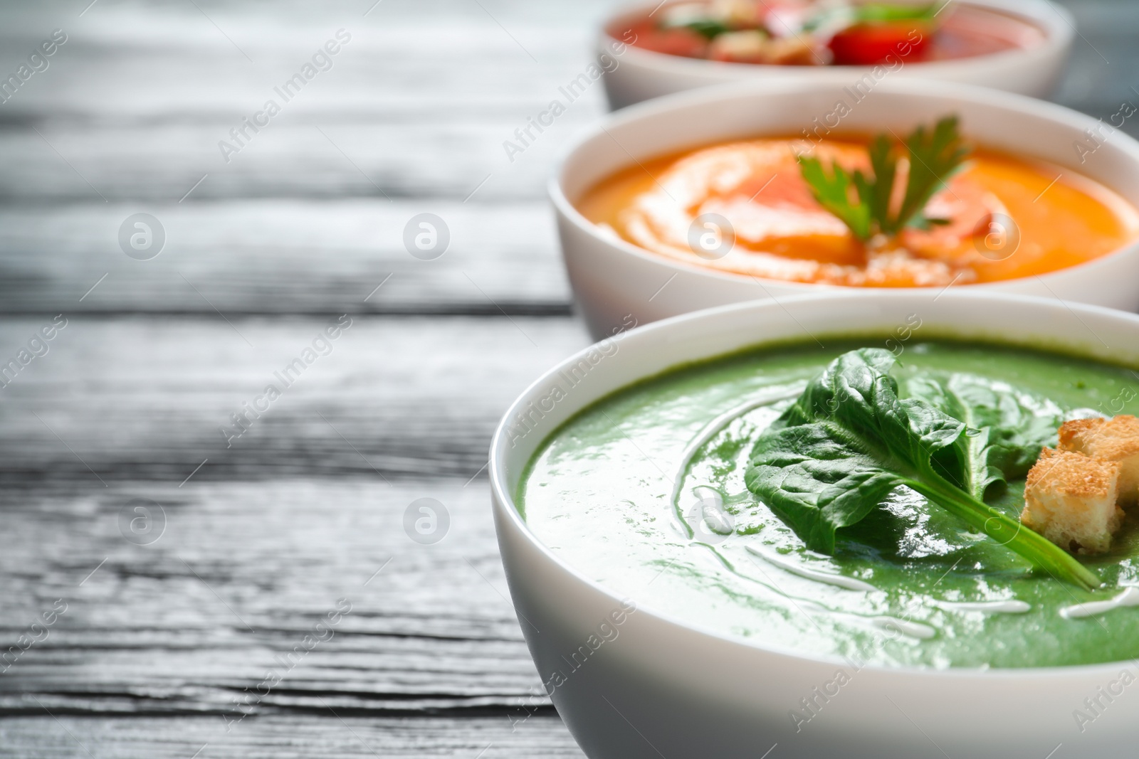 Photo of Various cream soups in bowls on wooden table. Space for text