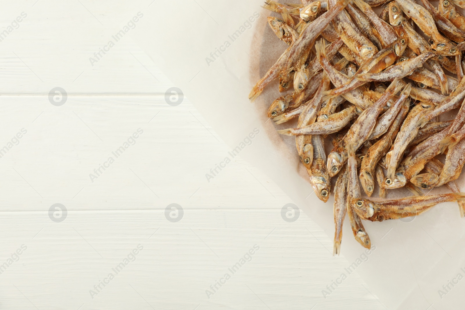 Photo of Tasty dried anchovies on white wooden table, top view. Space for text