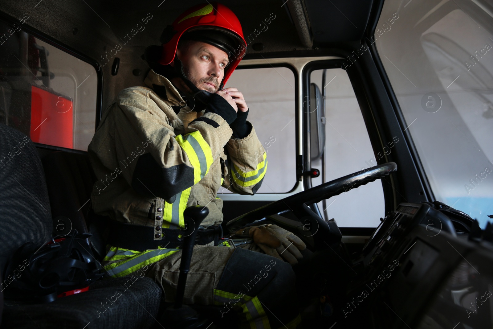 Photo of Firefighter in uniform wearing helmet inside fire truck