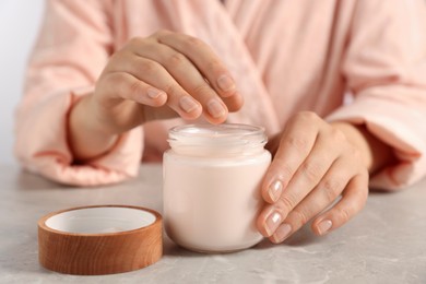 Photo of Woman applying hand cream at grey table, closeup