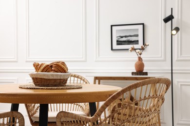 Photo of Tasty croissants on table and wicker chairs in dining room. Interior design