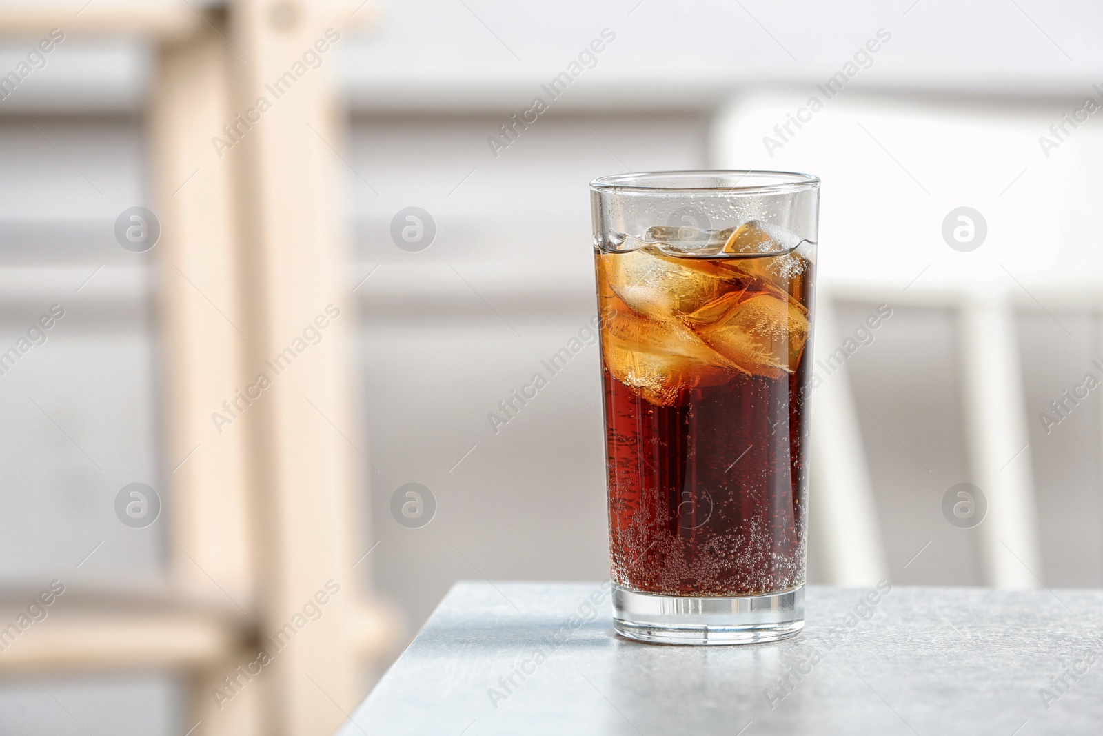 Photo of Glass of cold cola on table against blurred background. Space for text