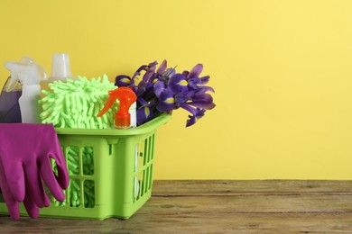 Photo of Spring cleaning. Basket with detergents, flowers and tools on wooden table. Space for text