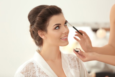 Photo of Makeup artist preparing bride before her wedding indoors