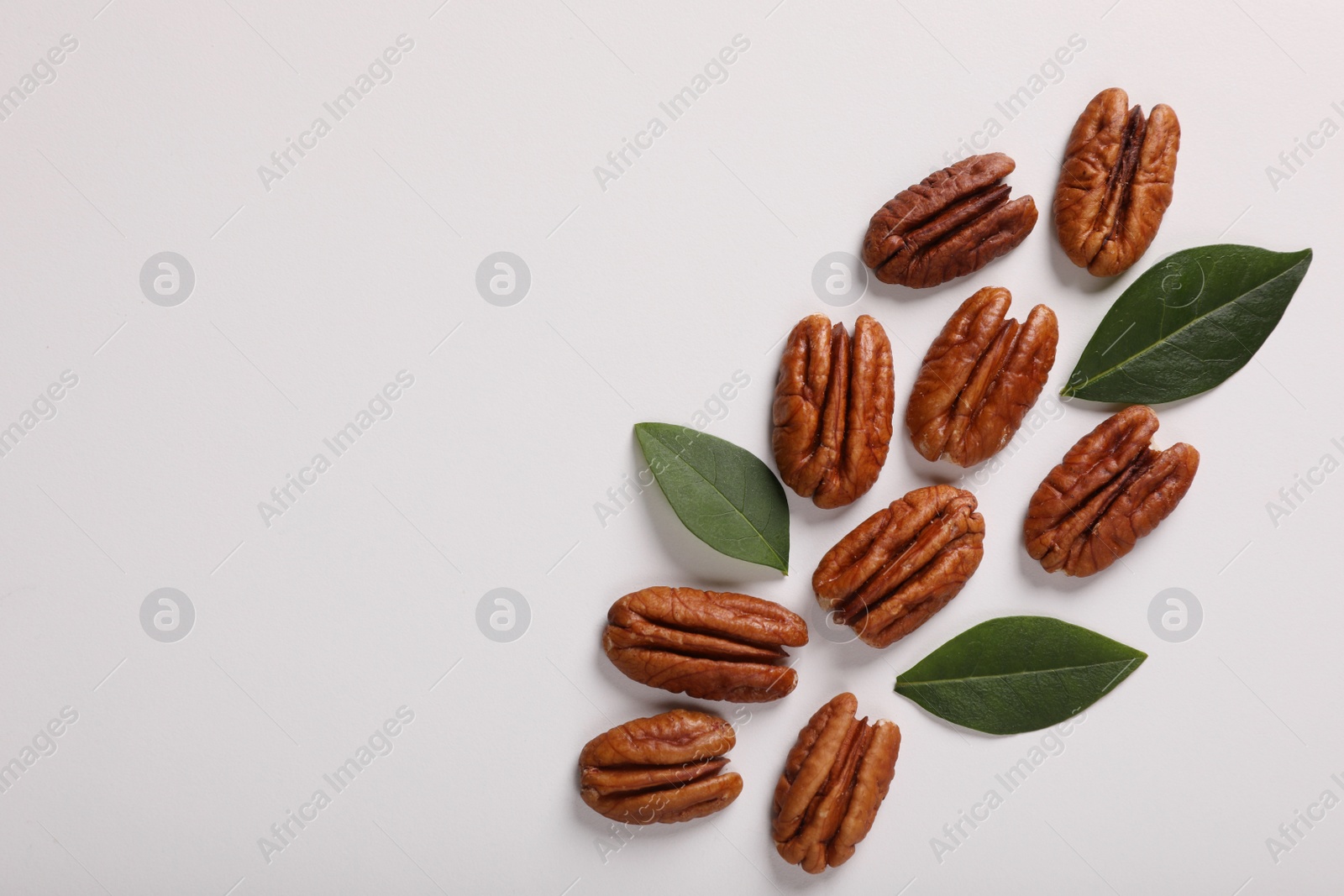 Photo of Delicious pecan nuts and green leaves on white background, flat lay. Space for text