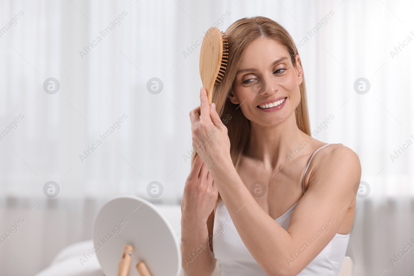 Photo of Beautiful woman brushing her hair near mirror in bedroom. Space for text