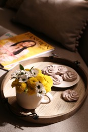 Tray with flowers in cup and delicious cookies on sofa indoors