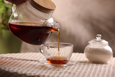 Photo of Woman pouring aromatic tea into cup at table, closeup