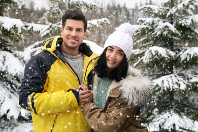 Happy couple near snowy fir trees outdoors. Winter vacation