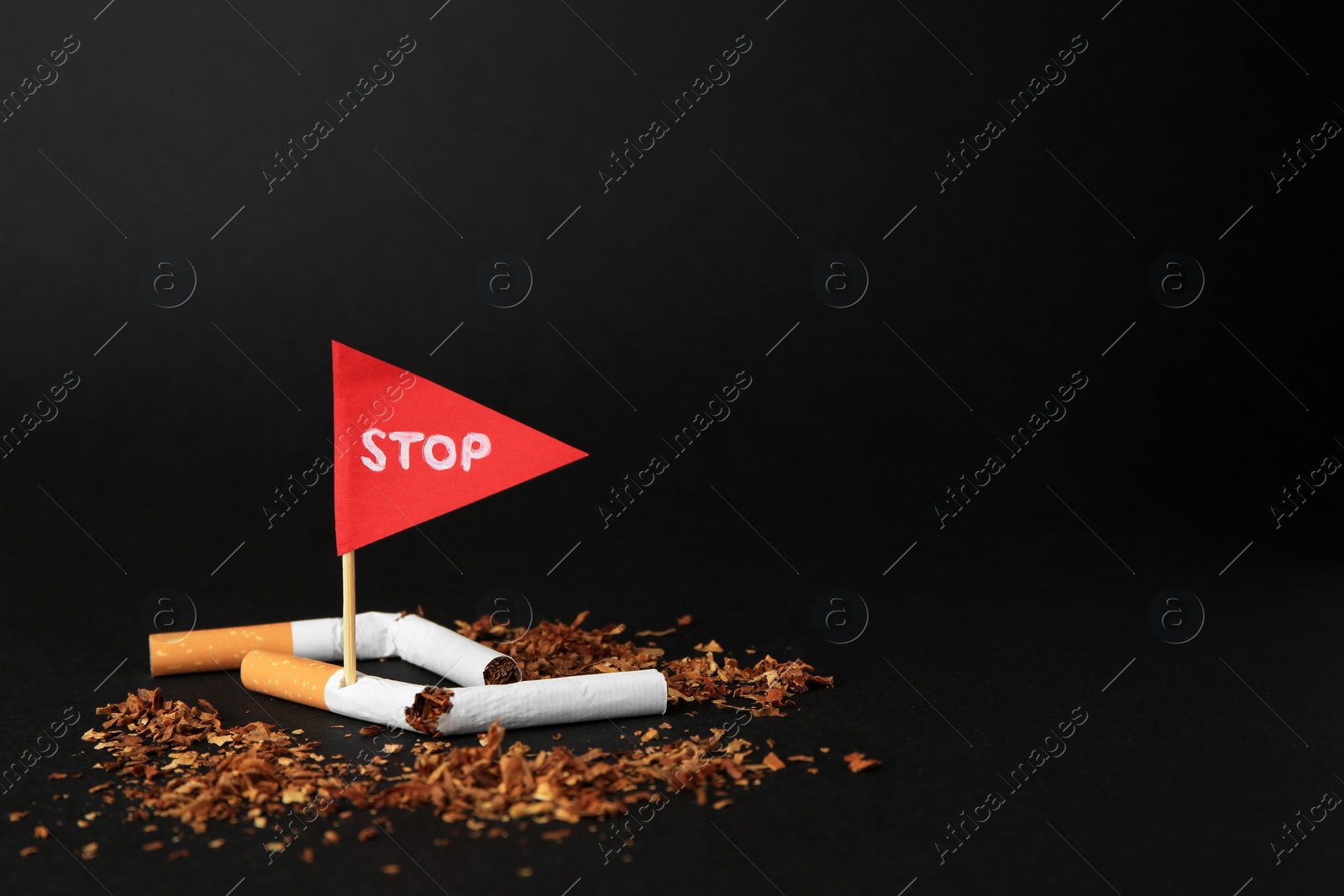 Photo of Broken cigarettes and red flag with word Stop on black background, space for text. Quitting smoking concept