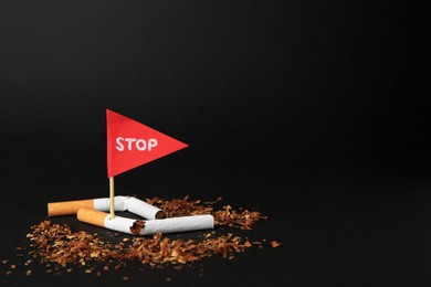 Broken cigarettes and red flag with word Stop on black background, space for text. Quitting smoking concept
