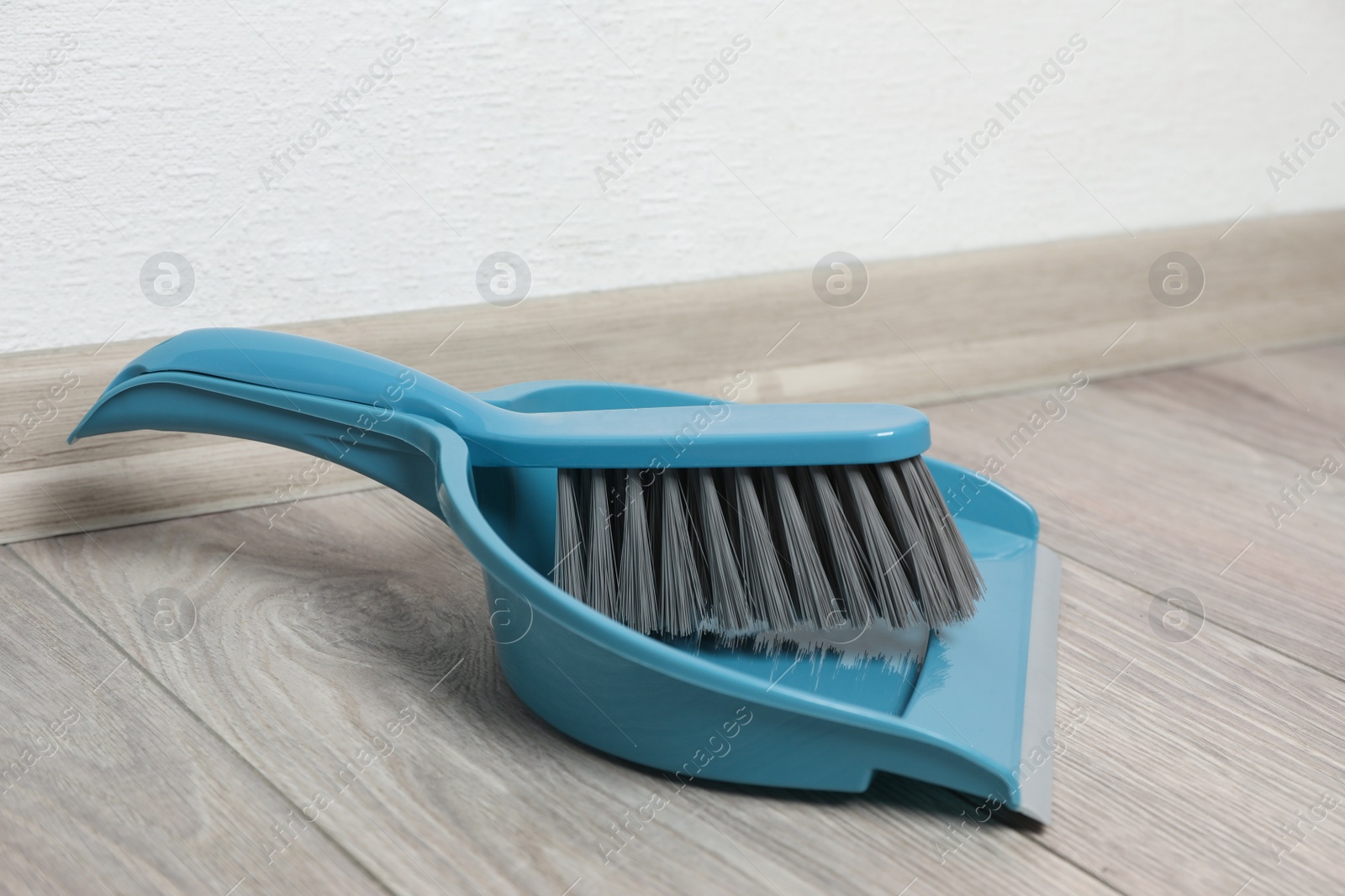 Photo of Plastic whisk broom with dustpan on wooden floor indoors