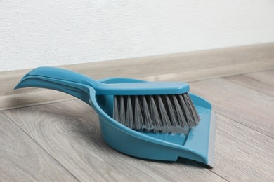 Photo of Plastic whisk broom with dustpan on wooden floor indoors