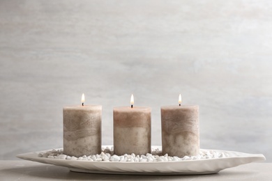 White plate with three burning candles and rocks on table