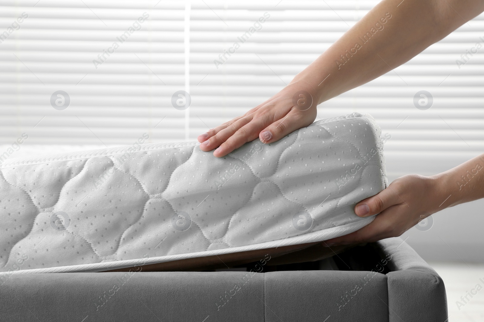 Photo of Woman putting soft light green mattress on gray bed indoors, closeup