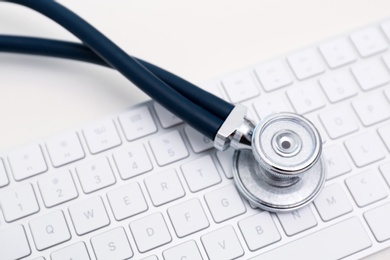 Photo of Modern keyboard and stethoscope on light background. Technical support concept