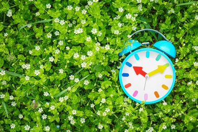 Photo of Alarm clock among flowers, outdoors. Time change concept