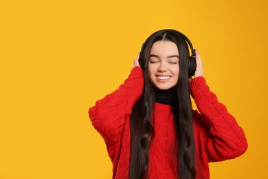 Photo of Teenage girl listening music with headphones on yellow background. Space for text