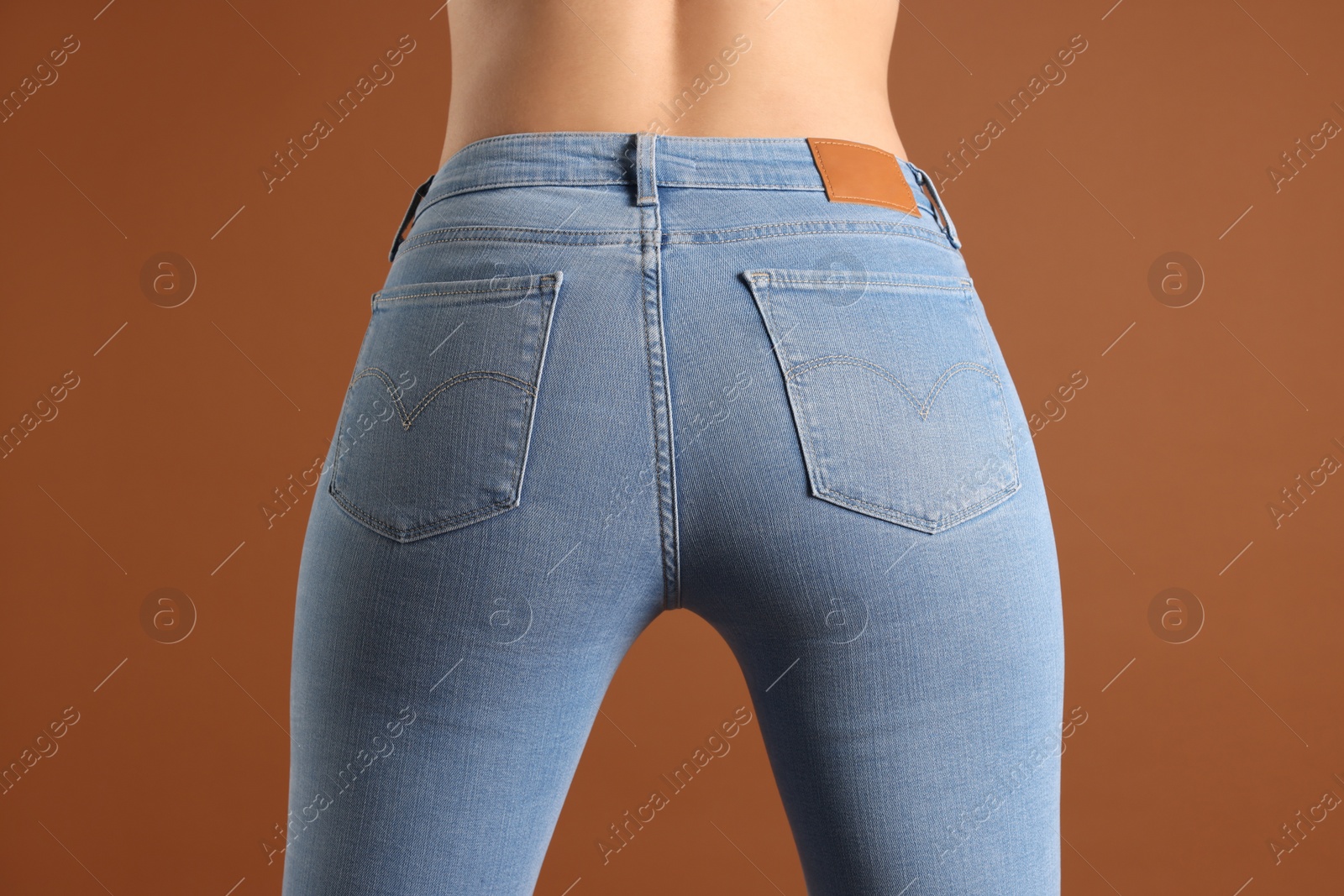 Photo of Woman wearing stylish light blue jeans on brown background, closeup