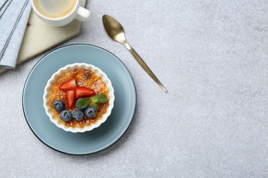 Photo of Delicious creme brulee with berries and mint in bowl served on grey textured table, flat lay. Space for text