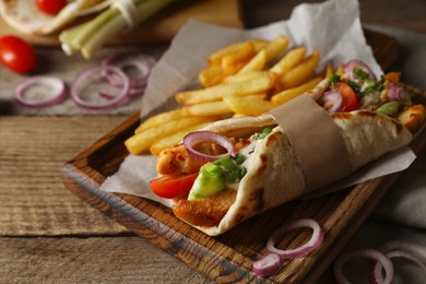 Delicious pita wrap with meat, vegetables and potato fries on wooden table, closeup