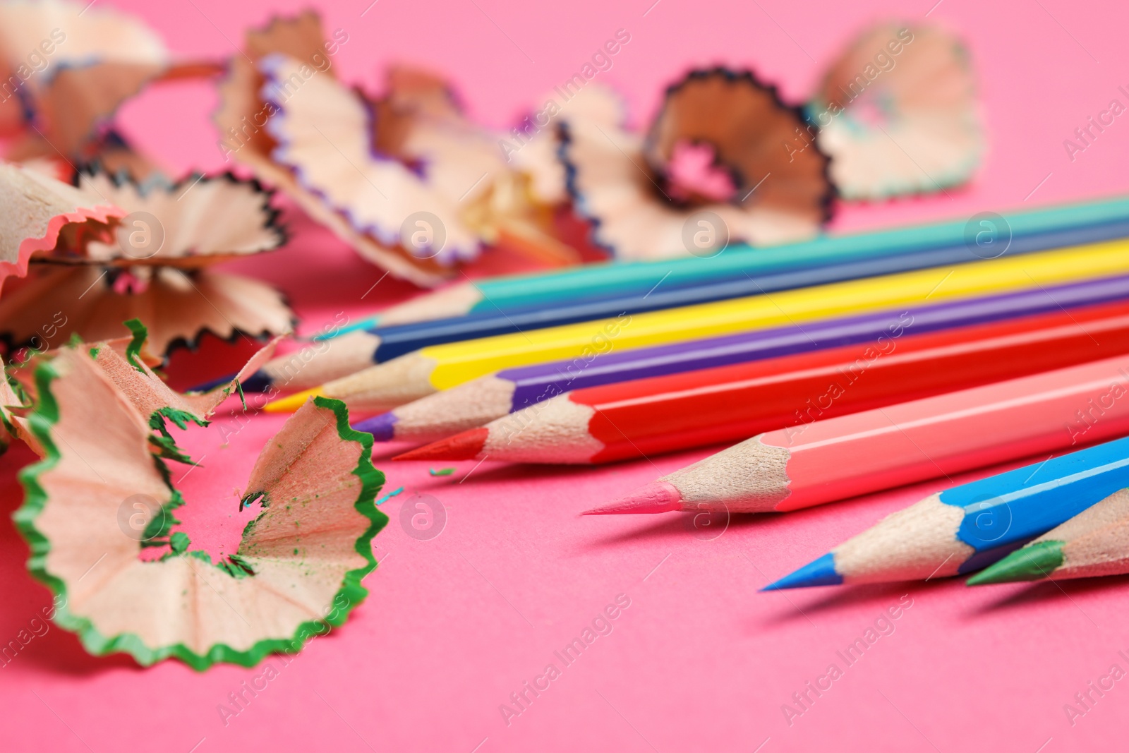 Photo of Color pencils and shavings on pink background, closeup