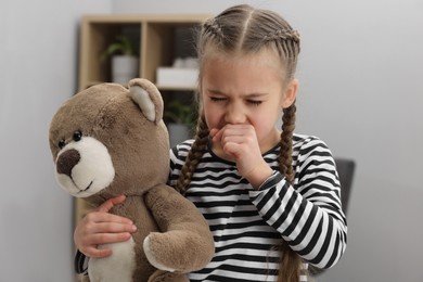 Sick girl with teddy bear coughing at home