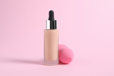 Photo of Bottle of skin foundation and sponge on pink background. Makeup product