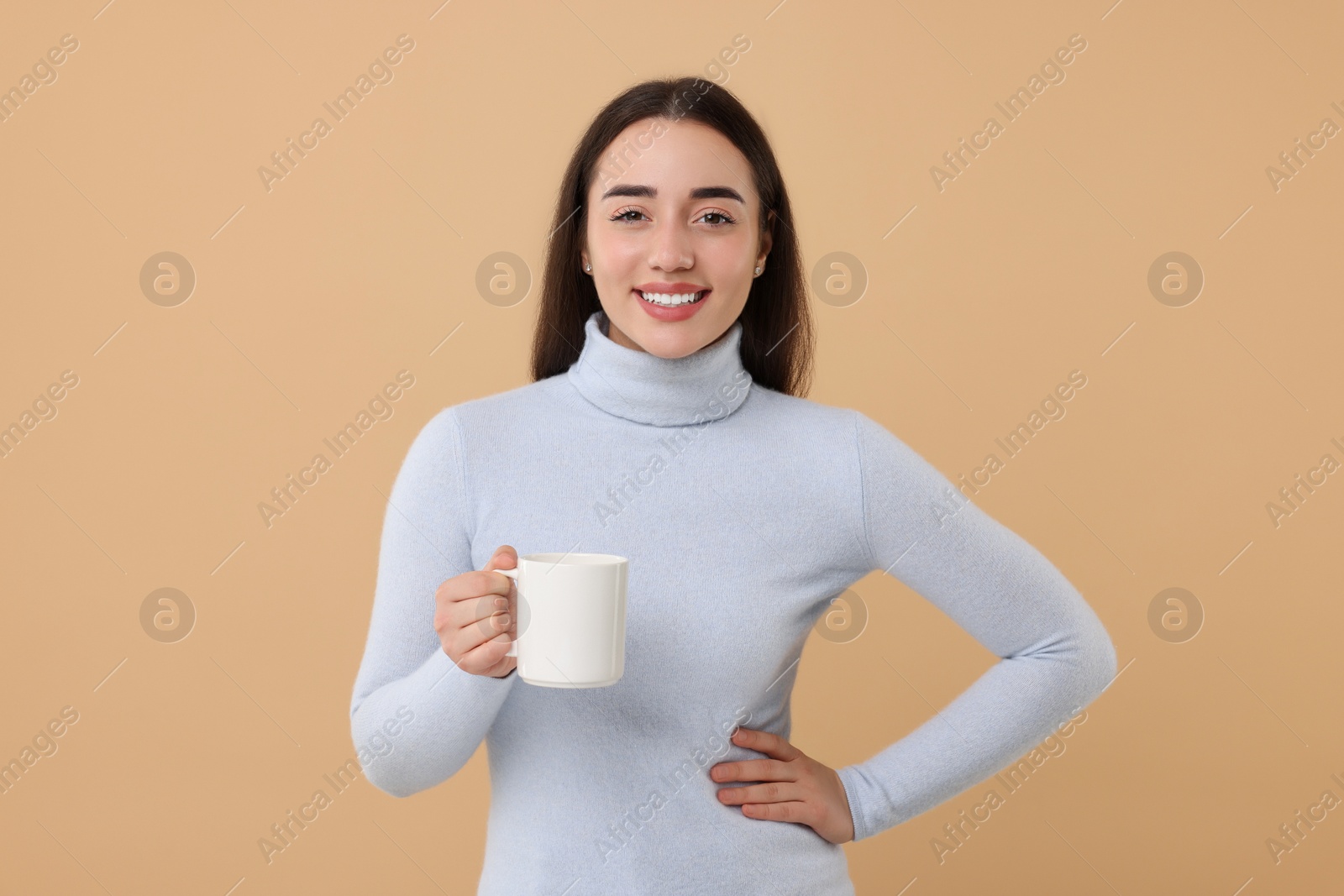 Photo of Happy young woman holding white ceramic mug on beige background