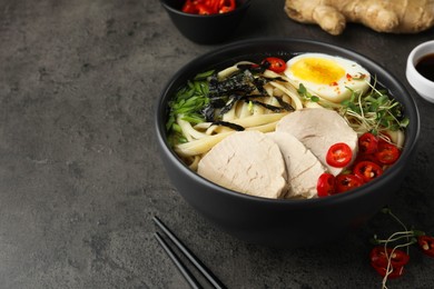 Delicious ramen with meat in bowl and ingredients on grey textured table, space for text. Noodle soup