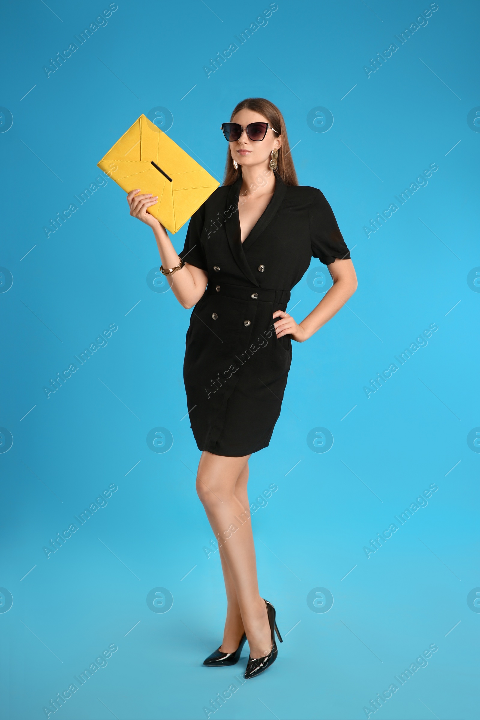 Photo of Beautiful young woman with stylish yellow bag on light blue background