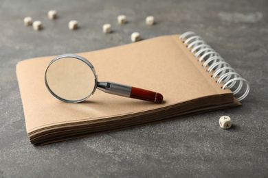 Photo of Magnifier glass, cube with letter A and empty notebook on grey stone background, closeup. Find keywords concept