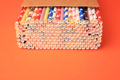 Photo of Box with many paper drinking straws on orange background