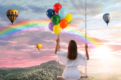 Image of Dream world. Young woman with bright balloons swinging, mountains under sunset sky on background