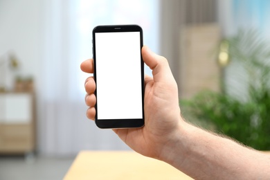 Photo of Man holding smartphone with blank screen indoors, closeup of hand. Space for text