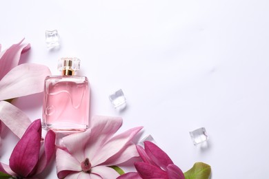 Beautiful pink magnolia flowers, bottle of perfume and ice cubes on white background, flat lay. Space for text